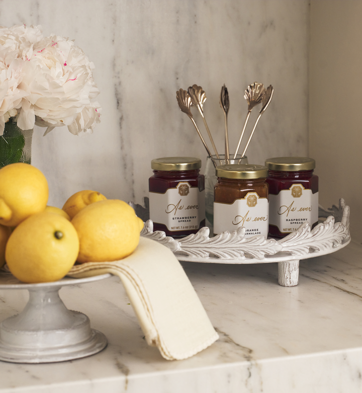 Jars of jam on a decorative stand with lemons and flowers on a marble surface