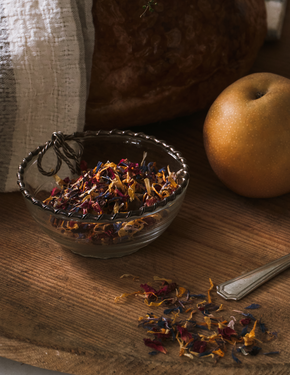 Glass bowl with flower sprinkles on a wooden surface next to an apple and a spoon.