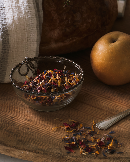 Glass bowl with flower sprinkles on a wooden surface next to an apple and a spoon.