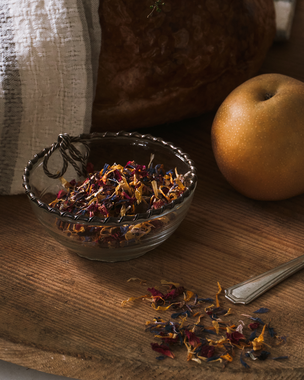 Glass bowl with flower sprinkles on a wooden surface next to an apple and a spoon.
