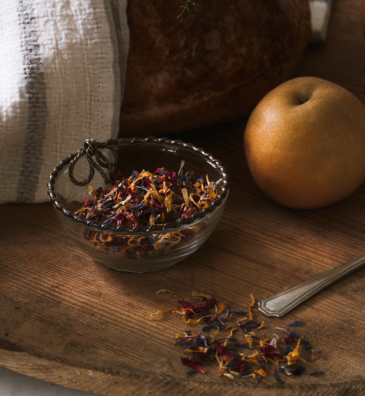 Glass bowl with flower sprinkles on a wooden surface next to an apple and a spoon.