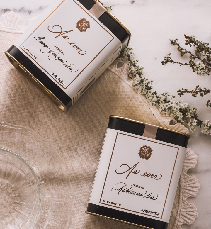 Two boxes of As ever herbal tea on a textured cloth surface with flowers.