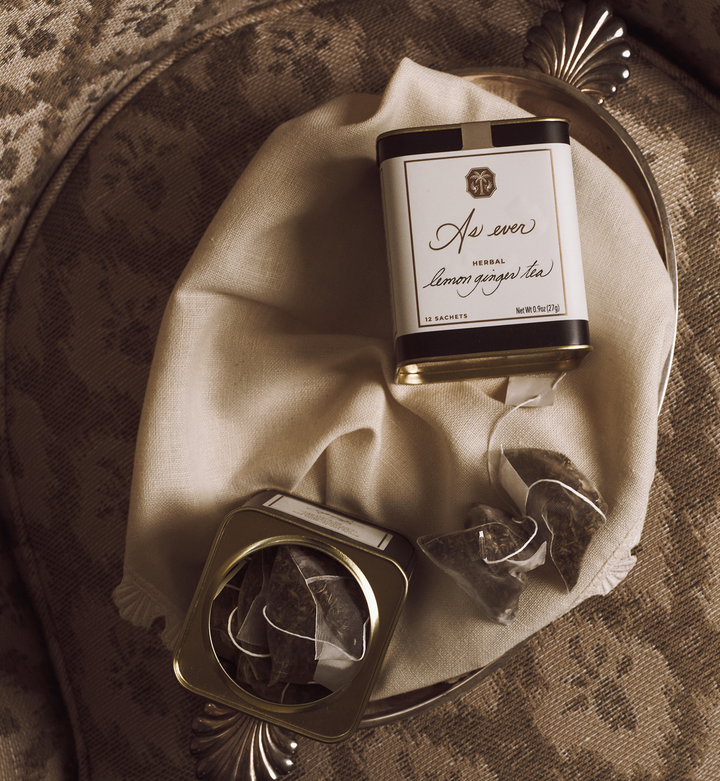 Tea canisters and tea bags on a decorative silver tray covered with a beige cloth. 