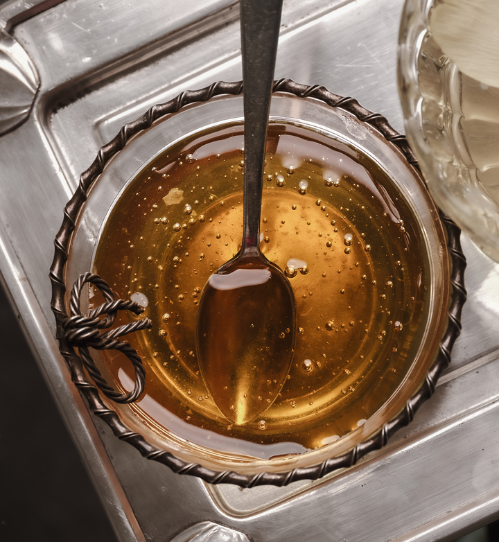 A glass filled with honey and a spoon on a decorative silver tray