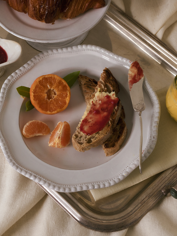 Breakfast setting with toast, orange slices, red fruit spread, and a glass of orange juice on a tray.