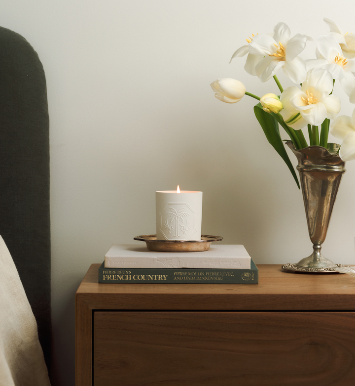 Candle on books with a vase of flowers on a wooden surface