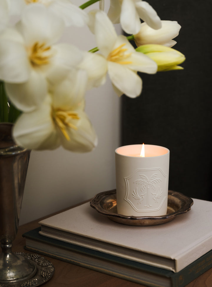 Candle with a decorative emblem on a stack of books next to white flowers.