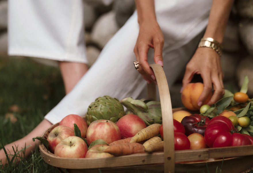 A woman reaching into a basket of vegetables and fruit. 