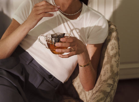Person holding a small cup of tea in a cozy indoor setting