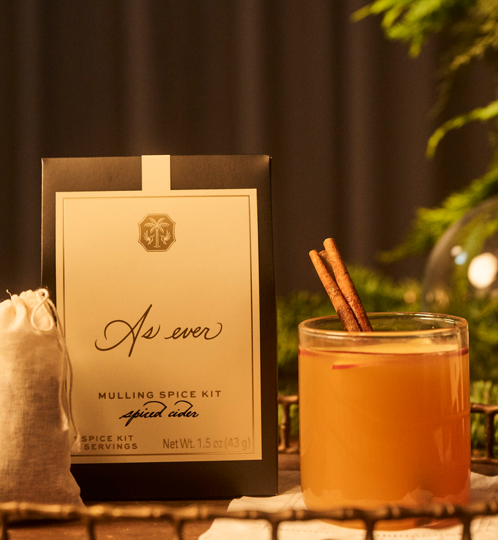 Mulling spice kit with a glass of spiced cider and cinnamon sticks on a tray.