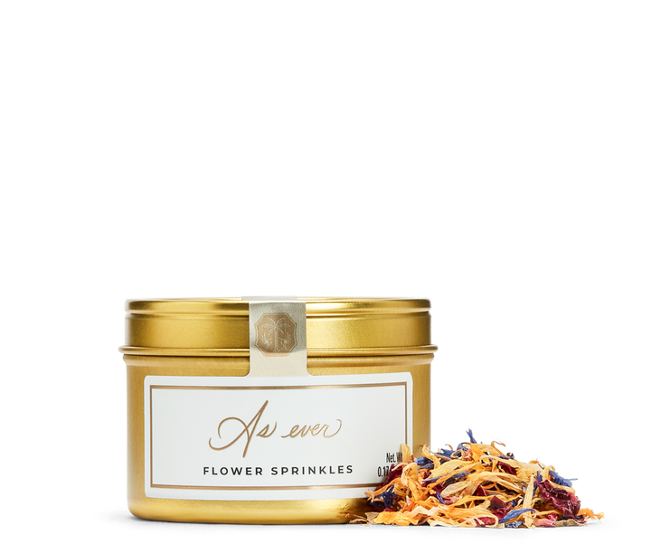 Gold tin of flower sprinkles with a decorative label, and loose flower sprinkles. 
