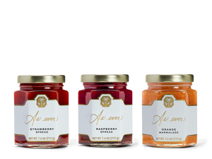 Three jars in a row, one with strawberry spread, one with raspberry spread, and one with orange marmalade. 