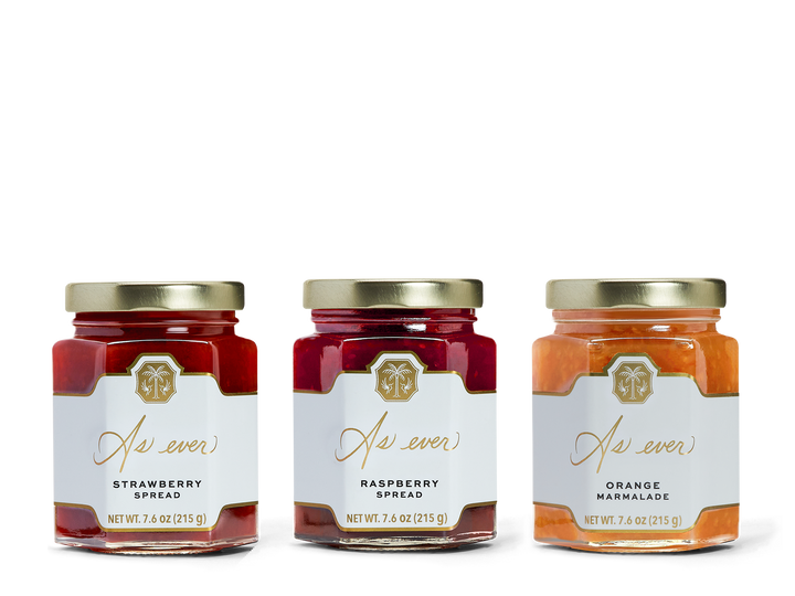 Three jars in a row, one with strawberry spread, one with raspberry spread, and one with orange marmalade. 