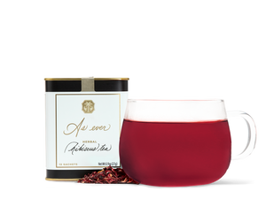 A tin of As ever tea, a clear glass of red tea, and loose dried tea leaves. 