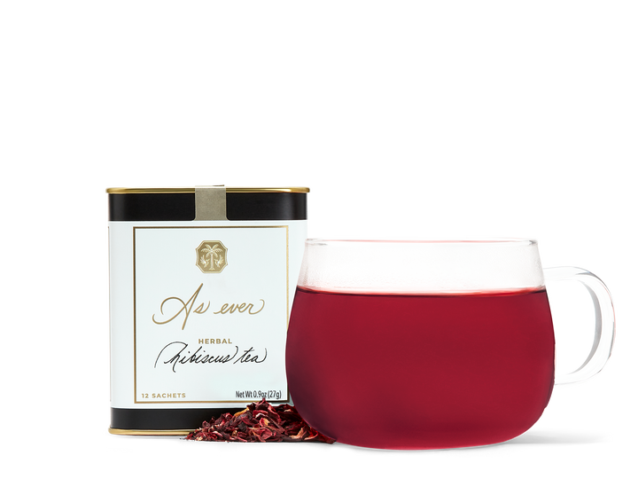 A tin of As ever tea, a clear glass of red tea, and loose dried tea leaves. 