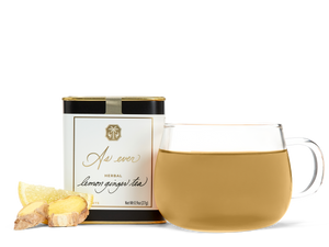 A tin of As ever tea, a clear glass of amber tea, and loose ginger and lemon slices. 