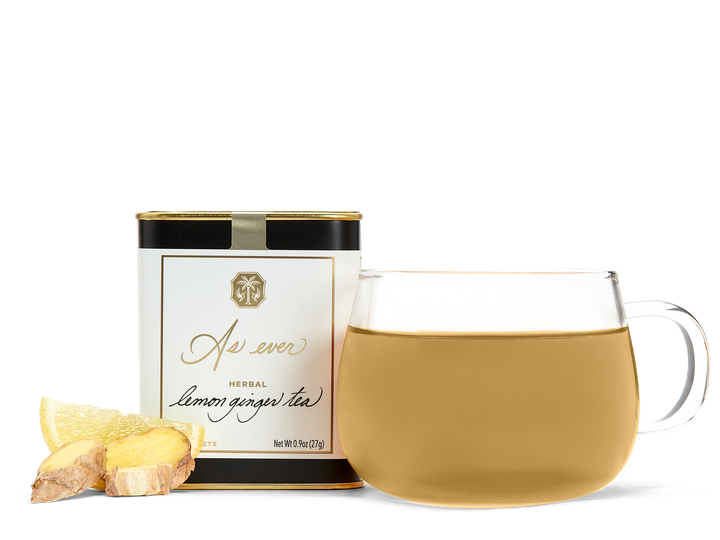 A tin of As ever tea, a clear glass of amber tea, and loose ginger and lemon slices. 
