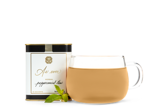 A tin of As ever tea, a clear glass of amber tea, and loose mint leaves. 