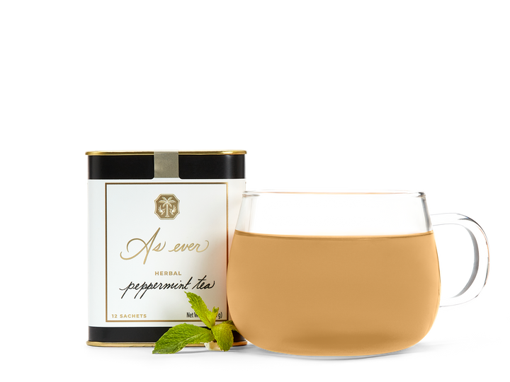 A tin of As ever tea, a clear glass of amber tea, and loose mint leaves. 