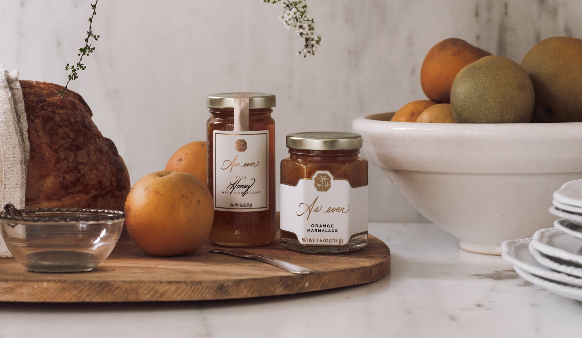 a jar of honey and orange marmalade of honey on a wooden board with apples and a bowl in the background.