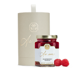 A jar of raspberry spread, raspberries, and a beige cylindrical box with gold detailing.