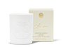 An unlit white candle with a decorative emblem beside a beige and gold candle box.