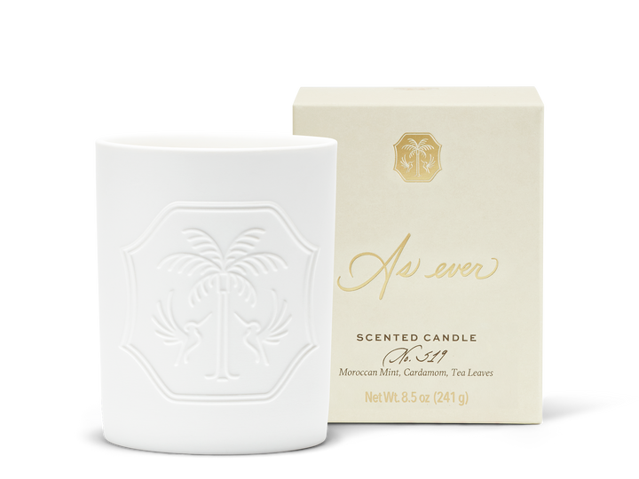 An unlit white candle with a decorative emblem beside a beige and gold candle box.