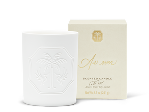 An unlit white candle with an engraved design beside a beige and gold candle box. 
