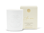 An unlit white candle with an engraved design beside a beige and gold candle box. 