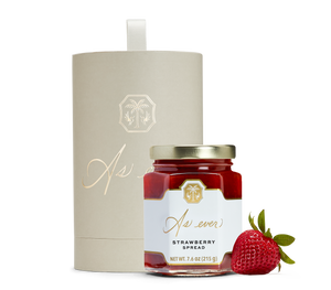 A jar of strawberry spread, a strawberry, and a beige cylindrical box with gold detailing. 