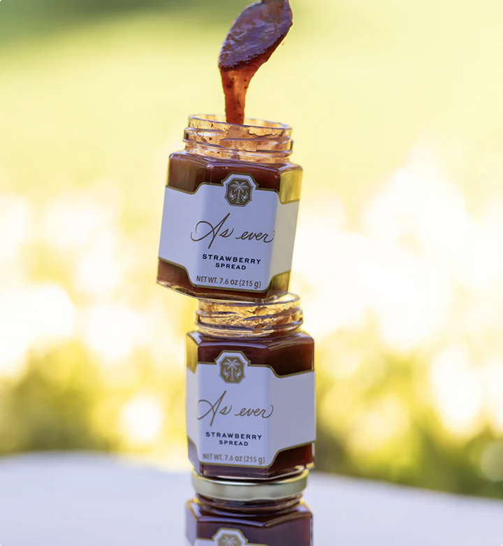 Two jars of strawberry spread with a dripping spoon against a blurred natural background