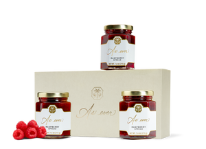 Three jars of raspberry spread, loose raspberries, and a beige box with a gold logo. 