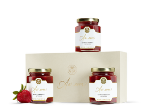 Three jars of strawberry spread, a strawberry, and a beige box with a gold logo.