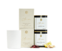 An unlit white candle beside two beige and gold candle boxes, two cans of As ever tea, and loose lemon, ginger, and hibiscus. 