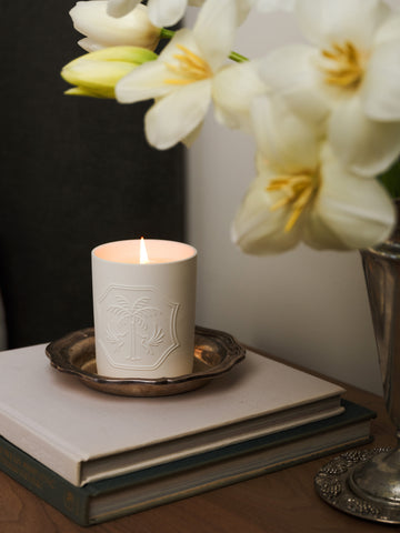White candle with decorative emblem on a stack of books, beside white flowers.