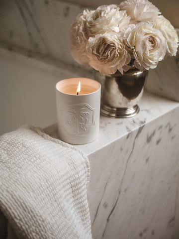 Lit white candle with a design and a silver vase of white flowers on a marble bathtub