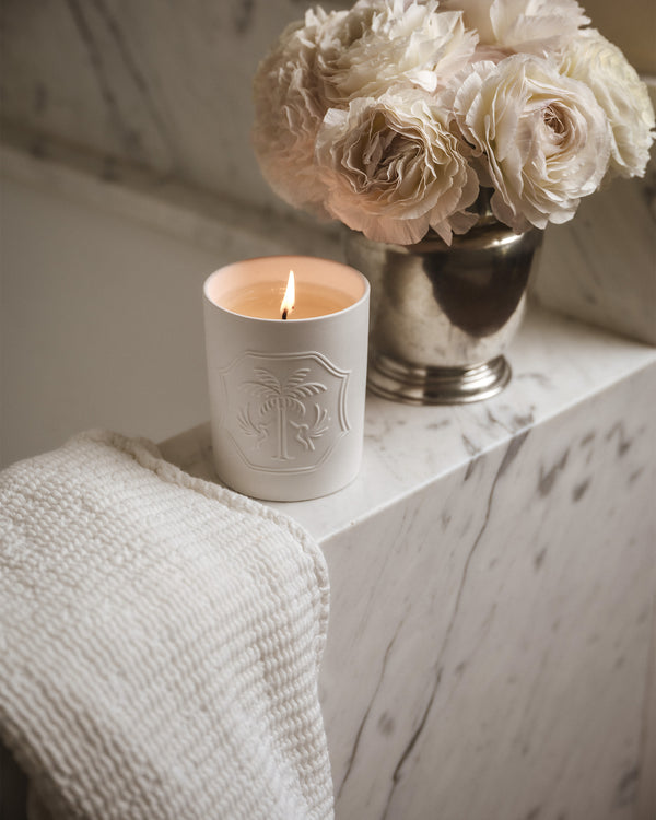 Lit white candle with a design and a silver vase of white flowers on a marble bathtub