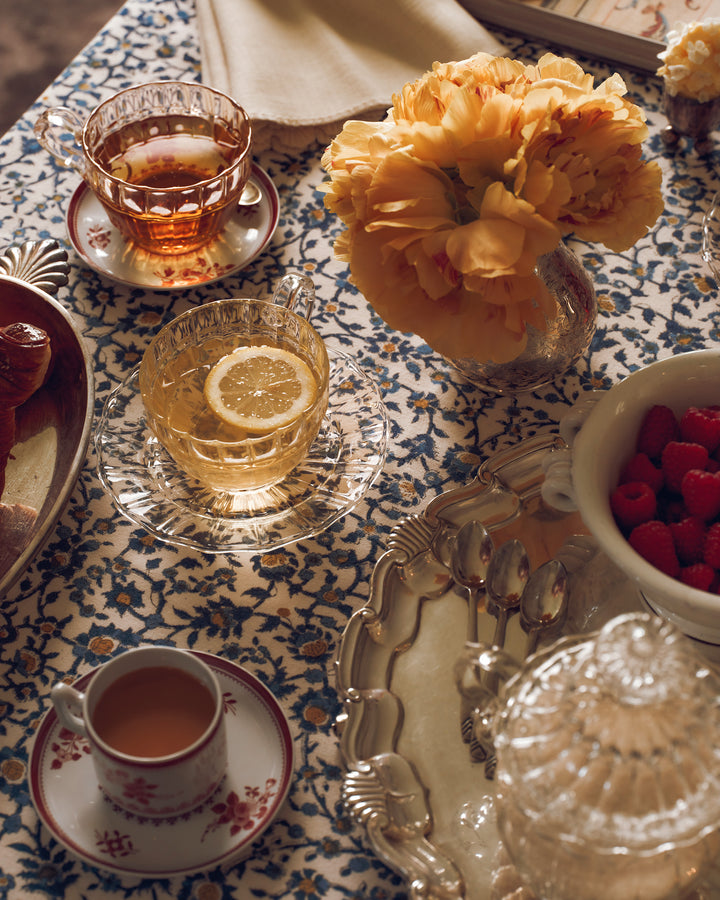 A table with a patterned tablecloth with tea and raspberries. 