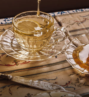 honey being dripped into Tea in a glass teacup with lemon slices on a decorative table.