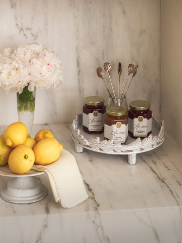 Three jars of jam sitting on a countertop with lemons. 