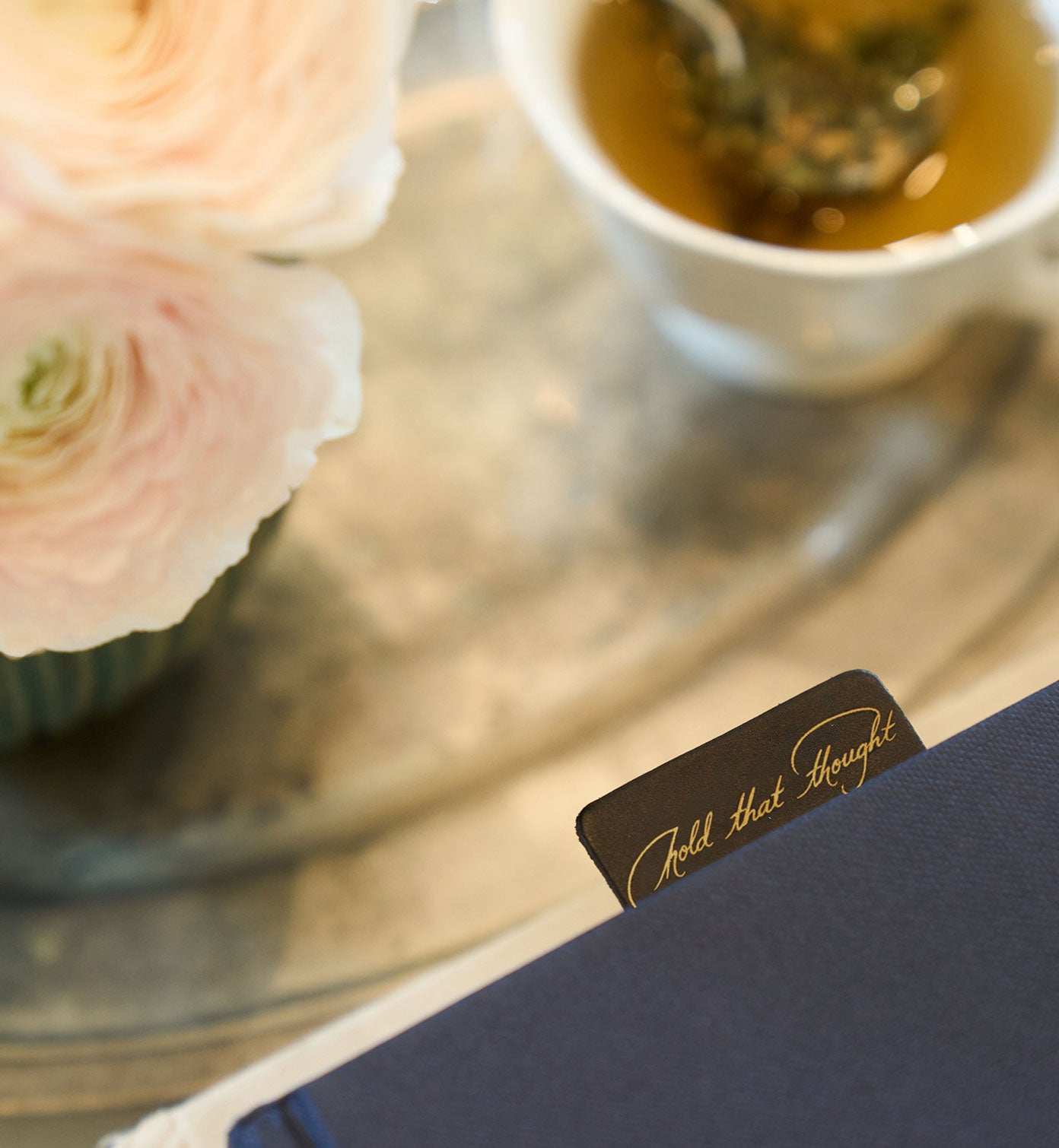 Teacup with pink flowers and a card on a reflective surface