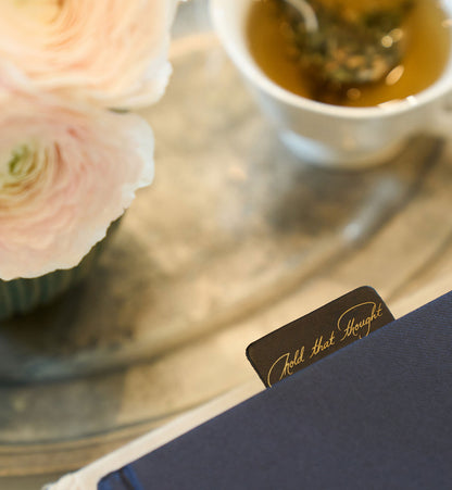 Teacup with pink flowers and a card on a reflective surface