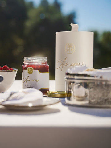 A jar of raspberry spreads sitting on the table in the sun. 