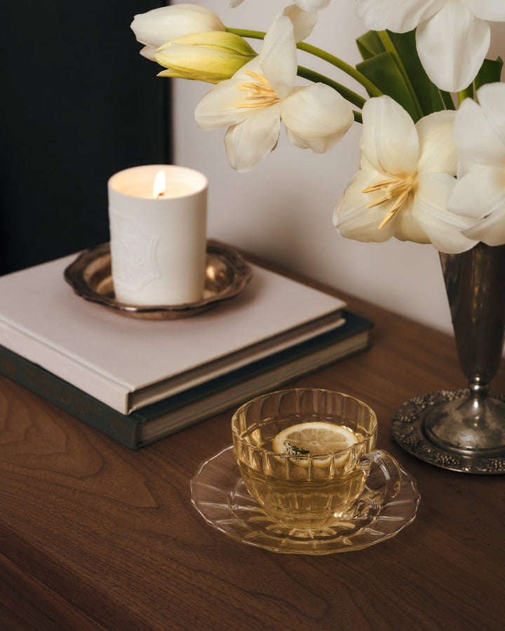A glass of tea on a wooden table with a candle and flowers. 